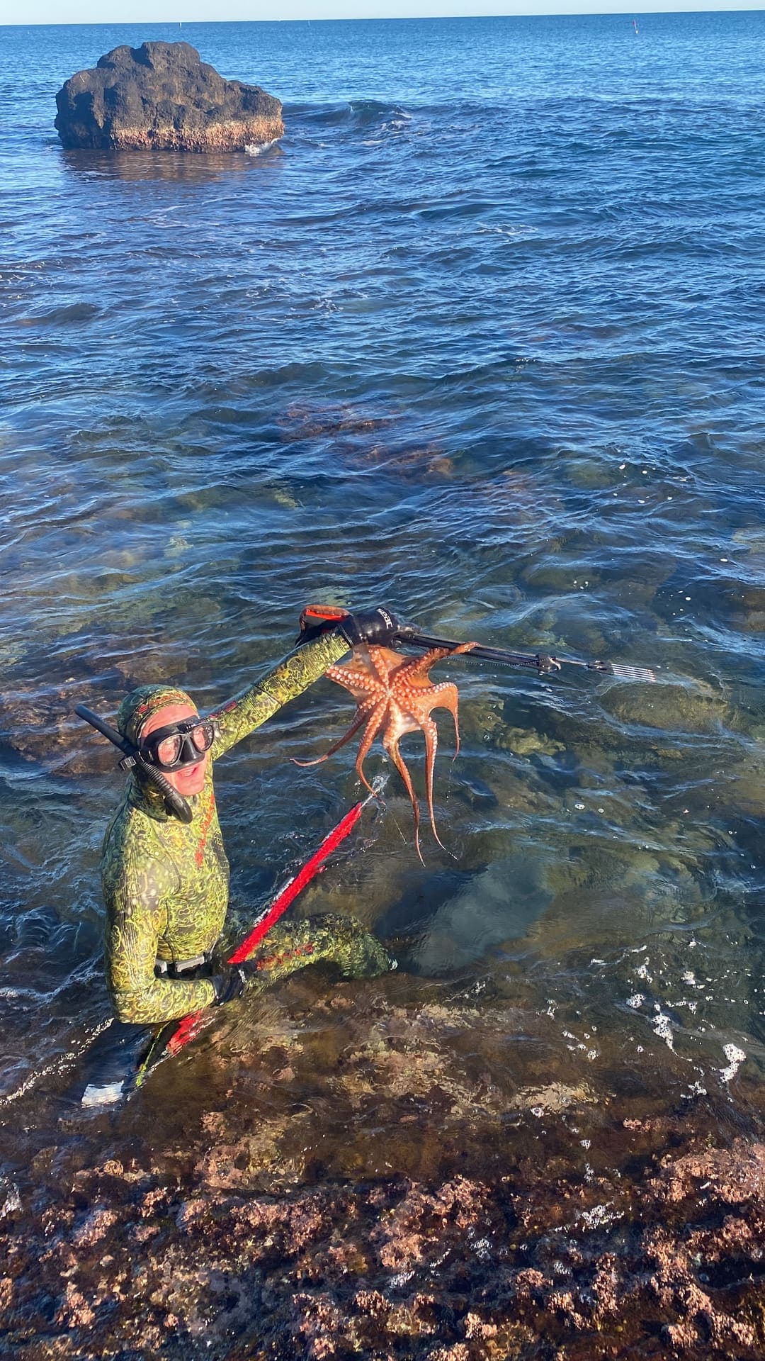 Justin dans l'eau près du bord, un poulpe et son fusil à la main