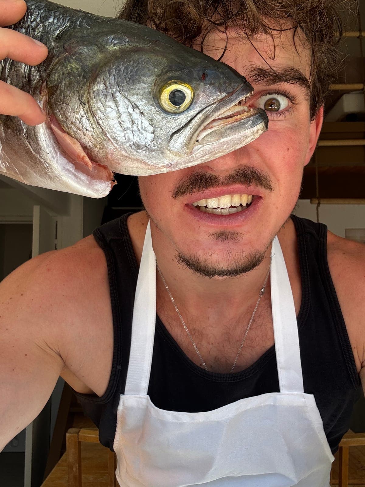 Justin en tablier, un poisson devant l'œil, dans sa cuisine